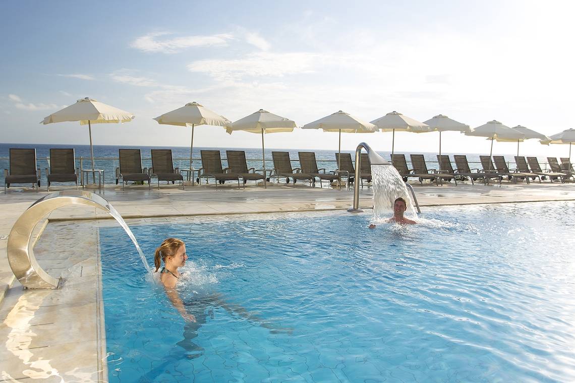Mensch schwimmt im Pool des Domes of Corfu, Autograph Collection mit Blick auf die Sonnenliegen