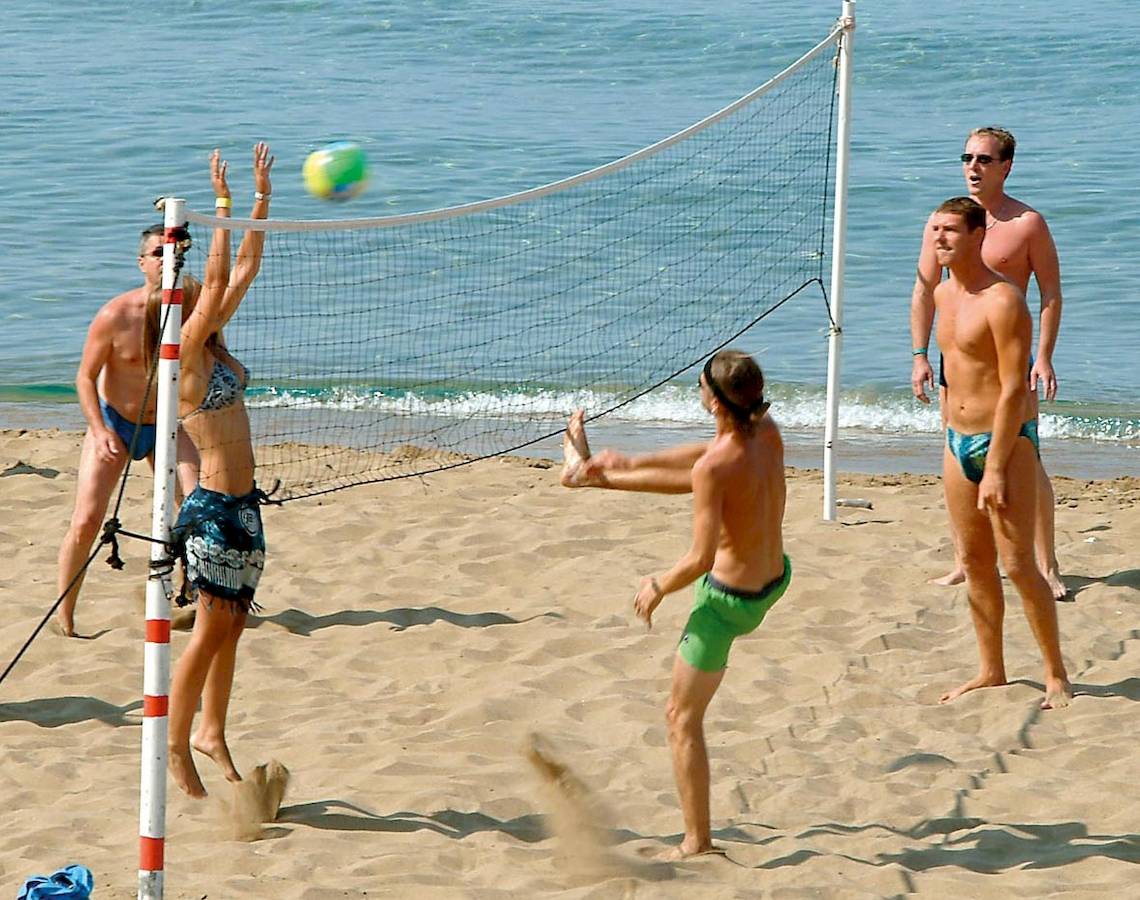 Gruppe junger Männer und Frauen spielt Volleyball am Strand in der Nähe des Wassers