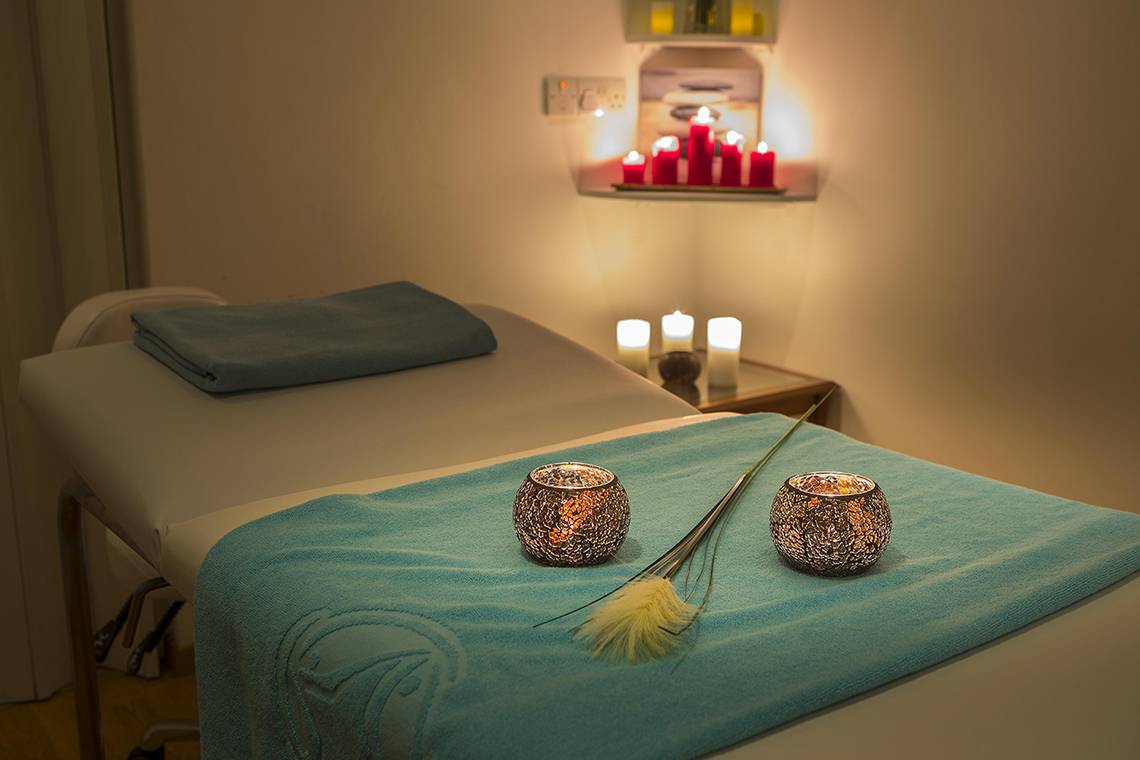 Massageraum im Lordos Beach Hotel mit blauen Laken, Kerzen und Pflanzen.