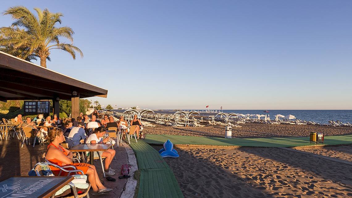 Wunderschoener Abend auf dem Strand im Miracle Resort mit vielen Menschen und Sonnenliegen.