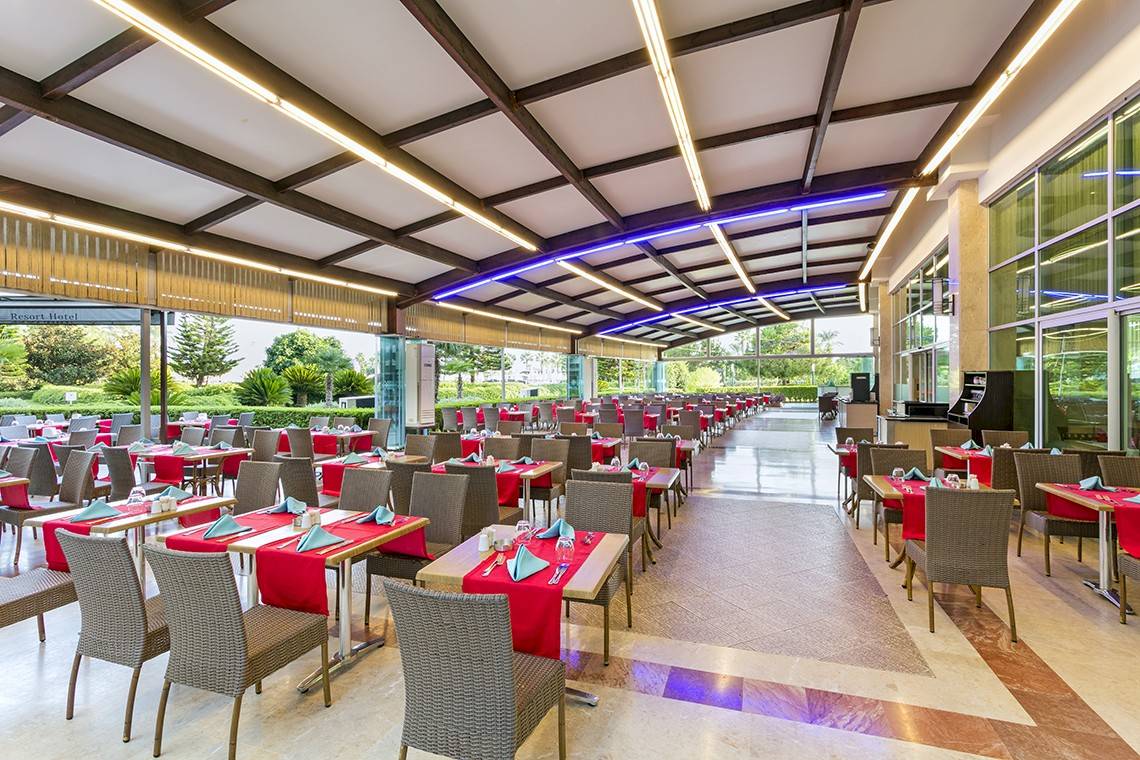 Restaurant des Miracle Resort mit vielen Tischen und roten Tischdecken, die in einer Reihe aufgestellt sind.