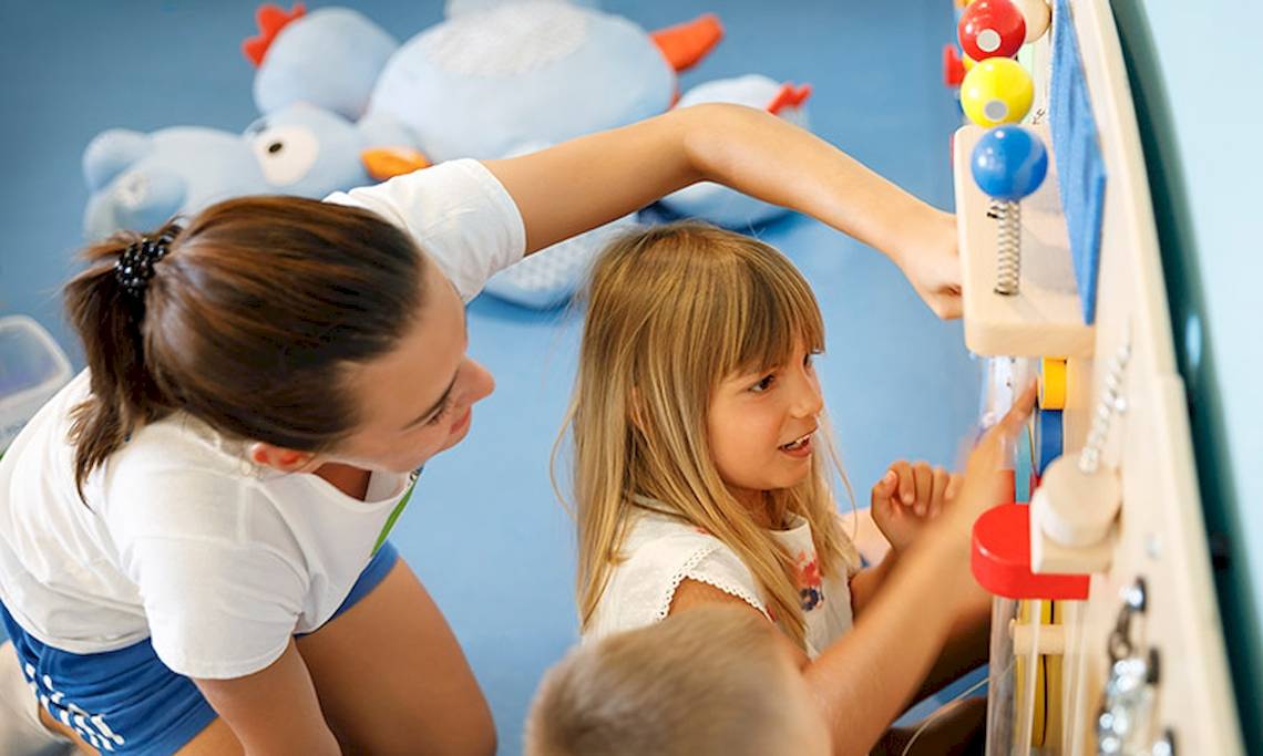 Eine Frau hilft einem Kind, eine bunte Spielwand im Club Dubrovnik Sunny Hotel zu nutzen.