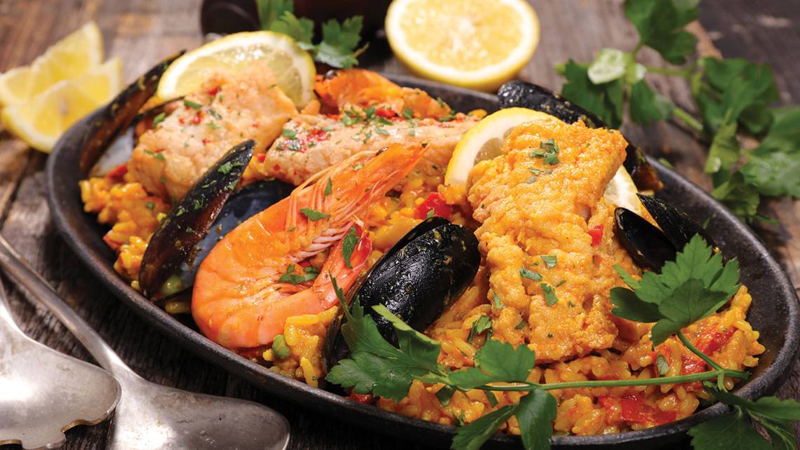 Eine traditionelle spanische Paella mit Garnelen, Muscheln und Zitrone serviert auf einem Holztisch.