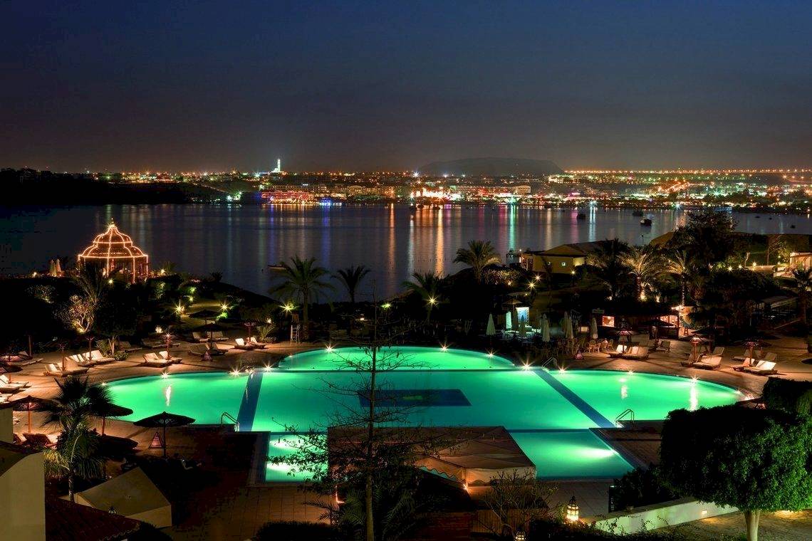 Nachtansicht des Moevenpick Resort Sharm el Sheikh mit beleuchtetem Pool und Stadt im Hintergrund