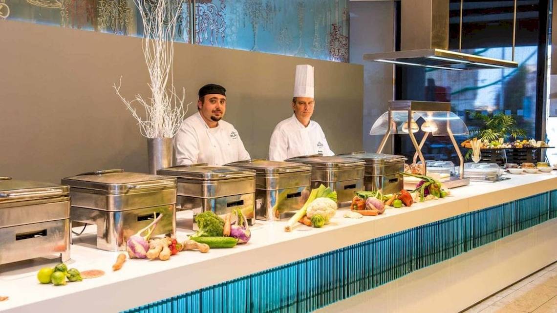 Zwei Köche in der Küche von AX The Palace, das Buffet ist voller Gemüse und Früchte.