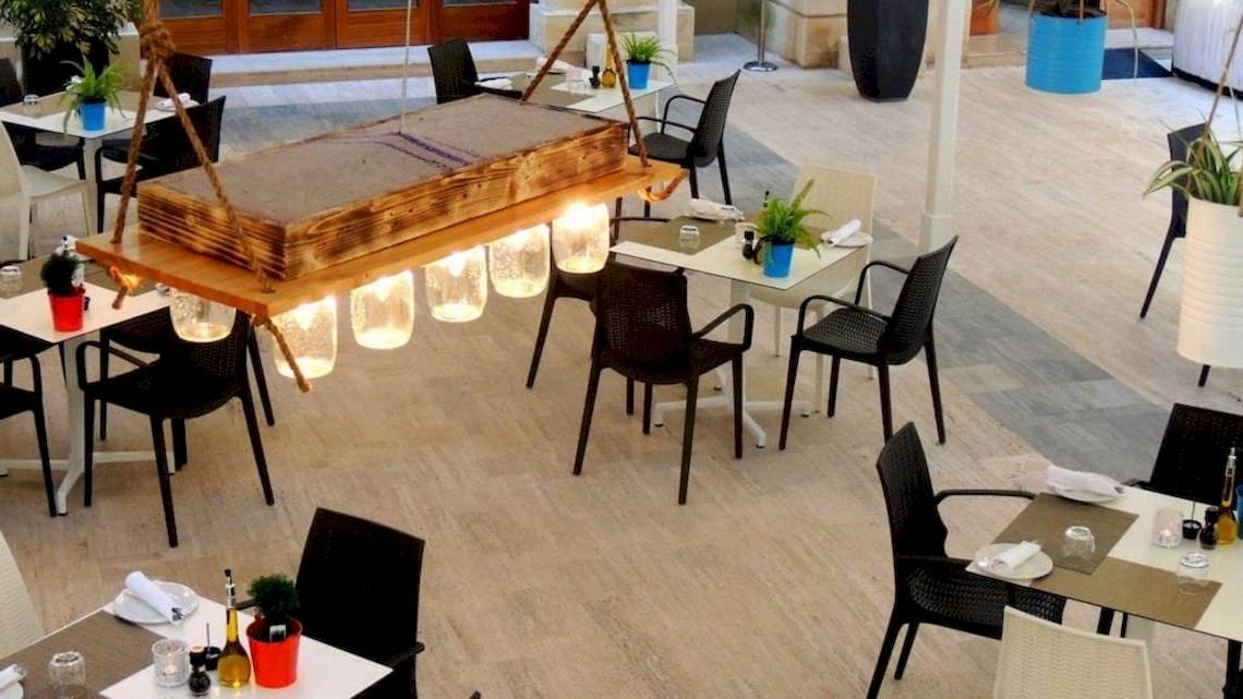 Innenansicht des Speisebereichs im AX The Palace Hotel mit Tischen, Stühlen und einer Holzleuchte.