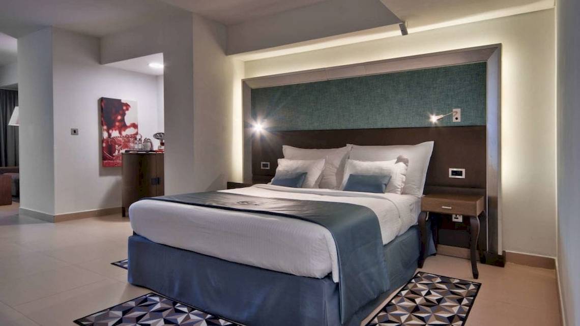 Innenansicht eines Hotelzimmers im AX The Palace mit einem großen Bett, Dekor und Nachttischen.