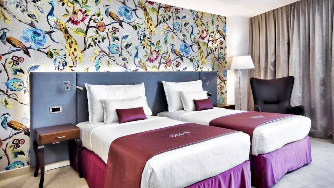 Doppelzimmer im AX The Palace mit zwei Betten und blumiger Tapete.
