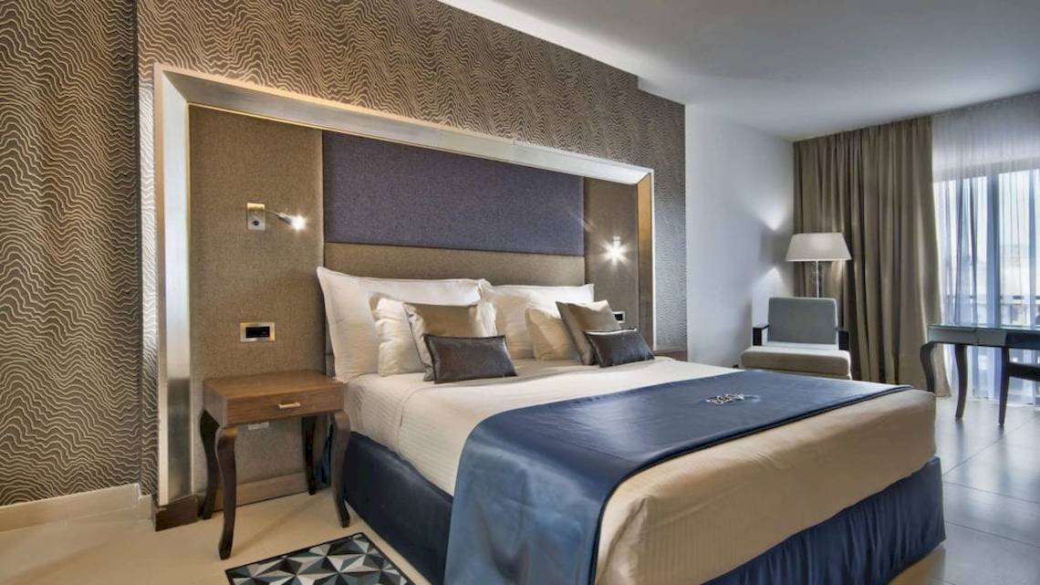 Hotelzimmer im AX The Palace mit einem großen Bett, Kissen, Tischlampe und Sessel.