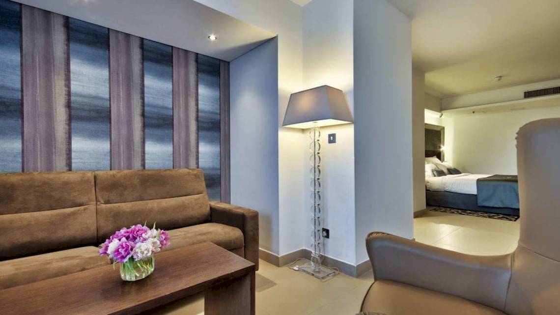 Innenansicht des AX The Palace Hotels mit Sofa, Tisch, Lampe und Schlafzimmer