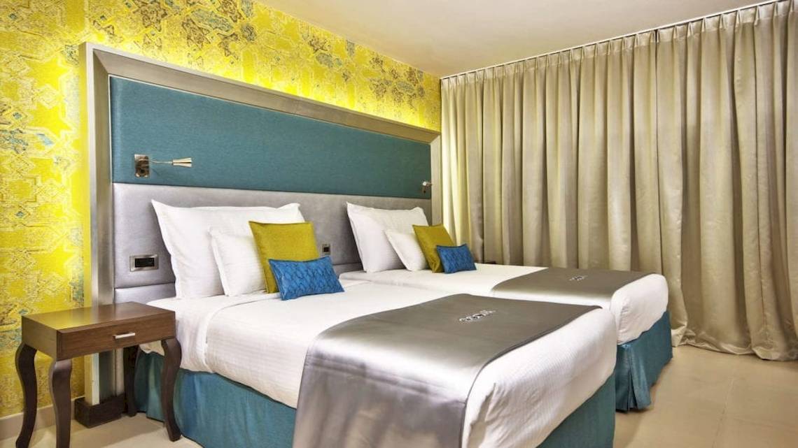 Zimmer im AX The Palace Hotel mit zwei Betten, blauen Kopfkissen und cremefarbenen Laken.