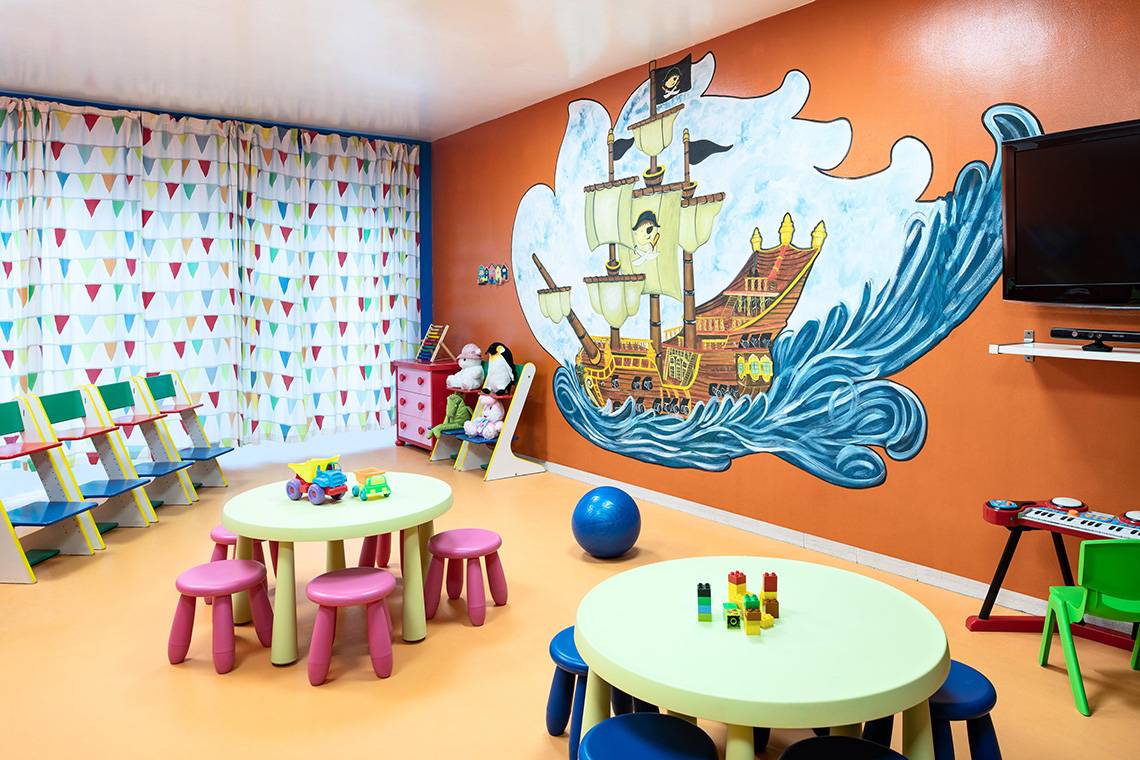 Kinderzimmer im Sheraton Jumeirah Beach Resort mit Piratenschiff-Wandmalerei und bunten Stühlen.