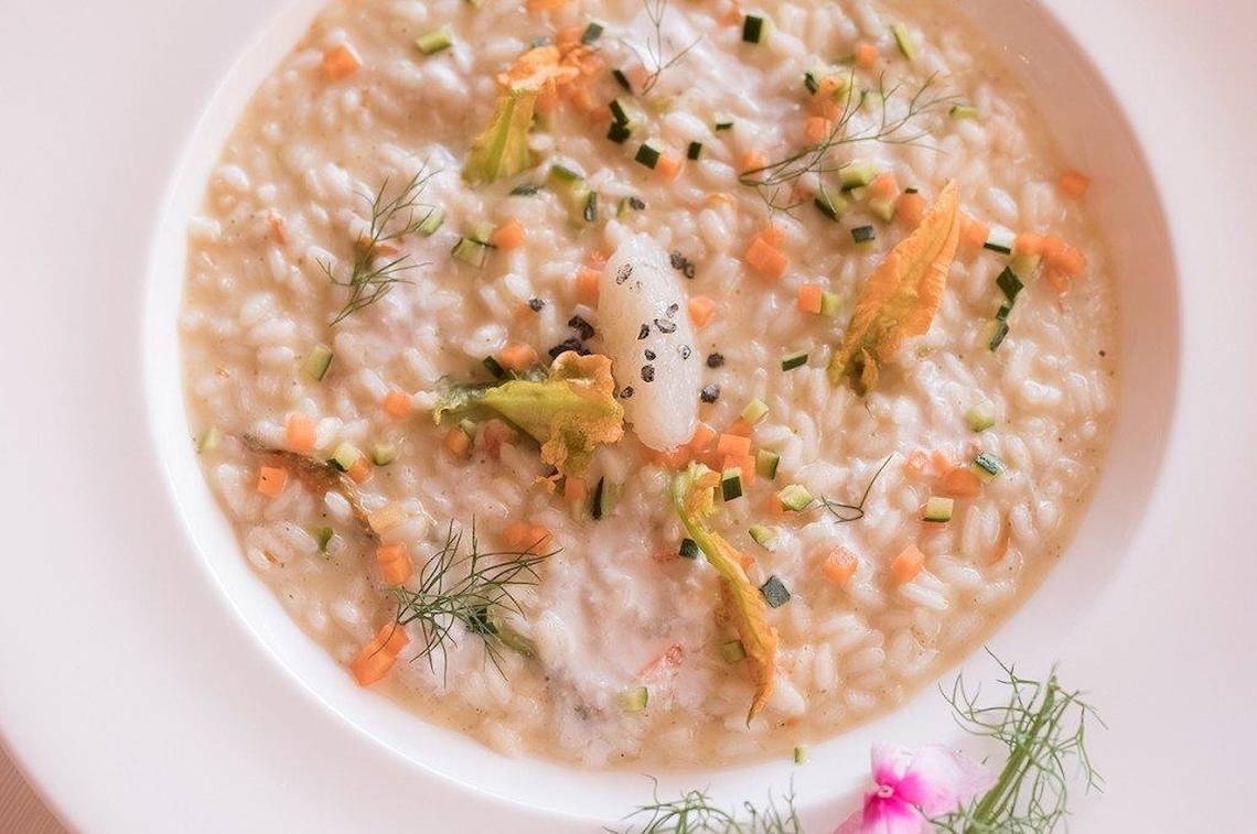 Eine Schüssel mit Risotto gefüllt mit Gemüse und Fisch, dekoriert mit Dill und Karotten.