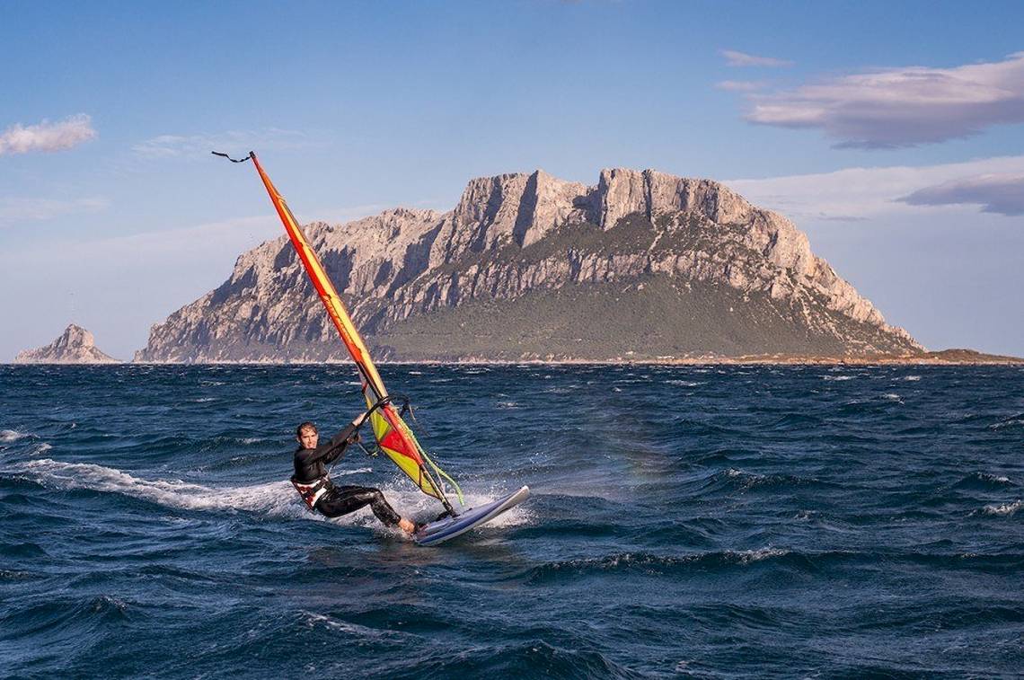 Windsurfer vor einer Insel mit Bergen im Hintergrund