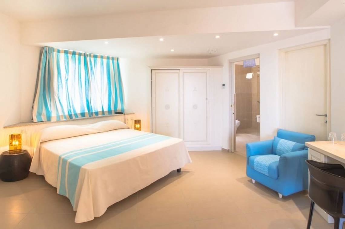 Schlafzimmer im Hotel Ollastu Resort mit Doppelbett, blauer Couch, Nachttischen und Lampen.