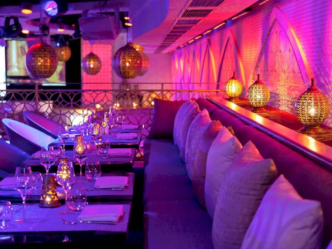 Innenbereich des Sofitel Marrakech Lounge mit blauer Beleuchtung, Sitzbänken und Tisch mit Gläsern und Servietten.