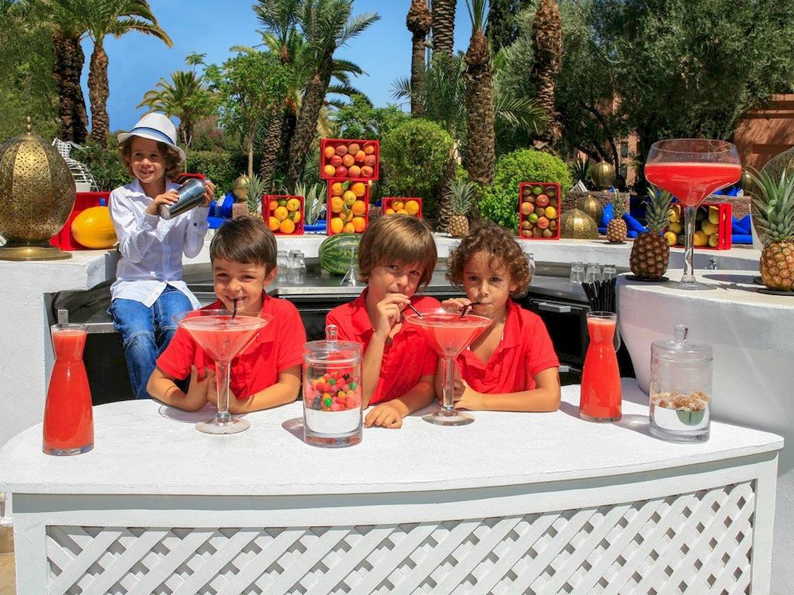 Kinder hinter einem Bartresen im Sofitel Marrakech Lounge & Spa mit selbstgemachten Getränken und Früchten im Hintergrund.