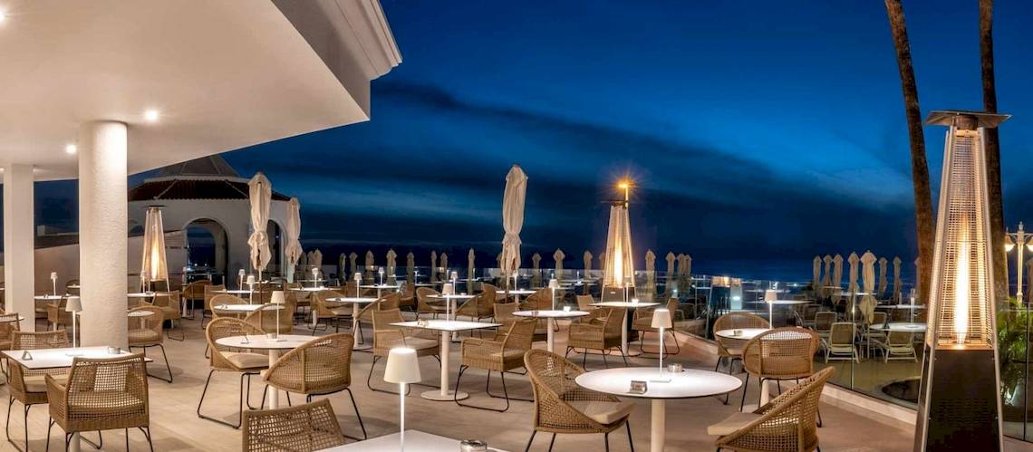 Außenbereich des Guayarmina Princess Hotels bei Nacht mit Tischen und Stühlen.