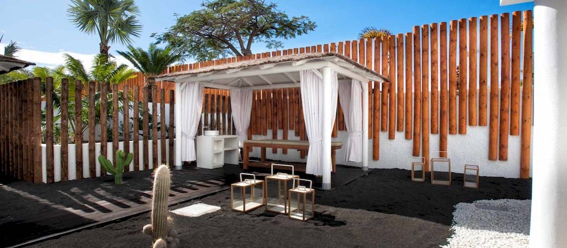 Außenbereich des Guayarmina Princess Hotels mit einem Pavillon, weißen Vorhängen und Holzzaun.