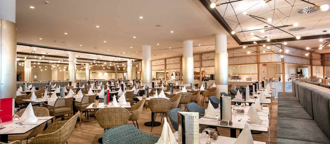 Innenbereich des Restaurants im Guayarmina Princess Hotel mit runden Tischen und Stühlen, dekorativen Lichtern und Holzboden.