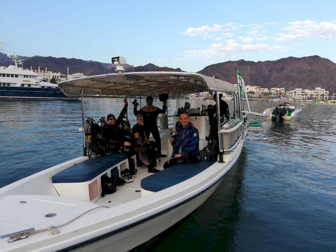 Taucher auf Boot vor Bergpanorama mit weiteren Booten im Hintergrund