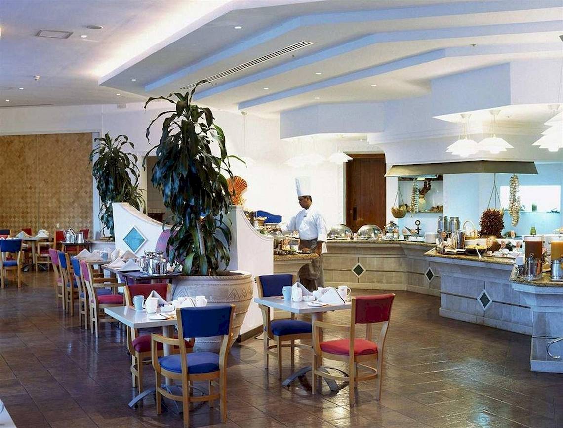 Innenansicht des Restaurants im Hilton Salalah Resort mit Tischen, Stühlen und einem Koch.