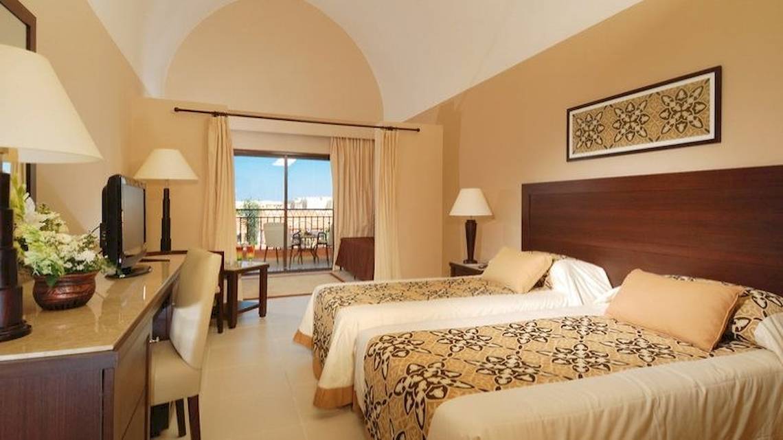 Hotelzimmer im JAZ Neo Dar El Madina mit zwei Betten, Fernseher, Schreibtisch und Balkon.