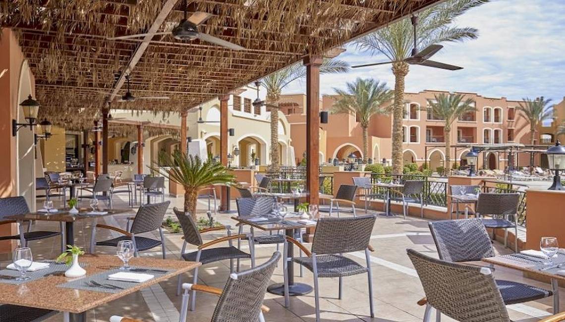 Restaurant-Terrasse im Jaz Neo Dar El Madina Hotel mit Tischen, Stühlen und Palmen im Hintergrund.