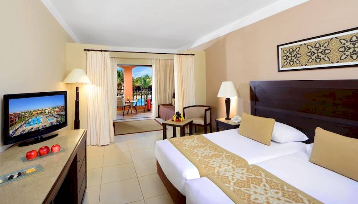 Doppelzimmer im Jaz Dar El Madina Hotel mit zwei Betten, Fernseher, und einem Balkon mit Blick auf den Pool.