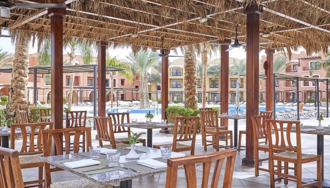 Außenbereich des Restaurants im JAZ Neo Dar El Madina Hotel mit runden Tischen und Stühlen unter einem Strohdach.