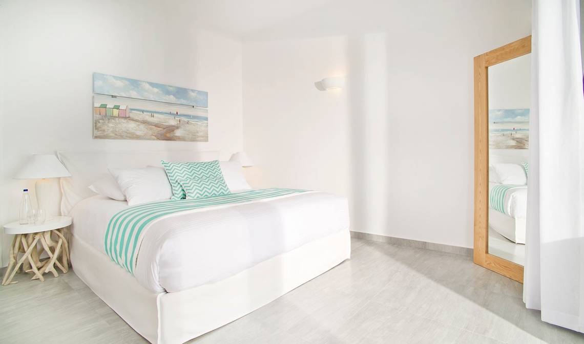 Innenansicht eines Hotelzimmers von Agali Houses mit weißem Bett, grünen Kissen und einer Wandmalerei.