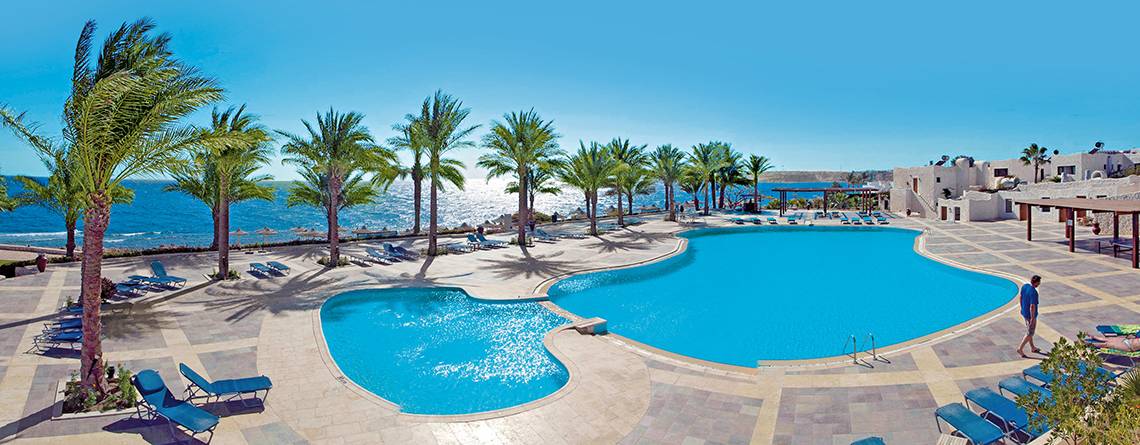 Poolbereich des Sharm Club Beach Resorts mit blauem Wasser und Palmen.