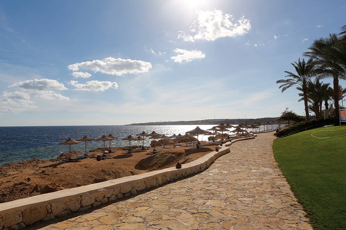Strandweg des Sharm Club Beach Resort mit Sonnenschirmen und Blick auf das Meer.