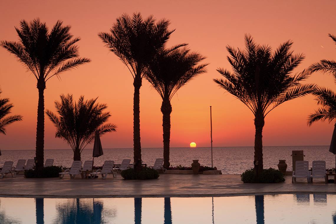 Sonnenuntergang am Pool von Sharm Club Beach Resort mit Palmen und Strandliegen.