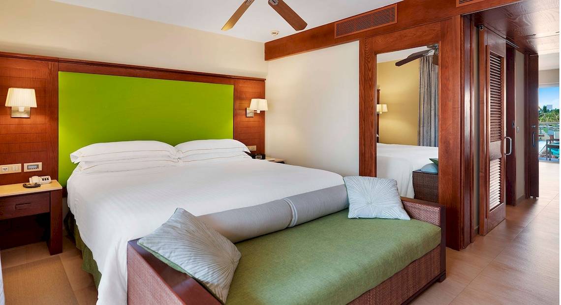 Schlafzimmer im Barcelo Bavaro Palace Hotel mit grüner Kopfseite, weißen Bettlaken und einer grünen Bank.