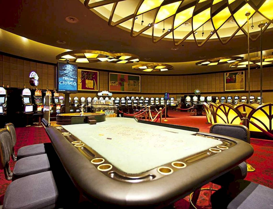 Ein Casino mit einem leeren Spieltisch und Spielautomaten im Hintergrund.