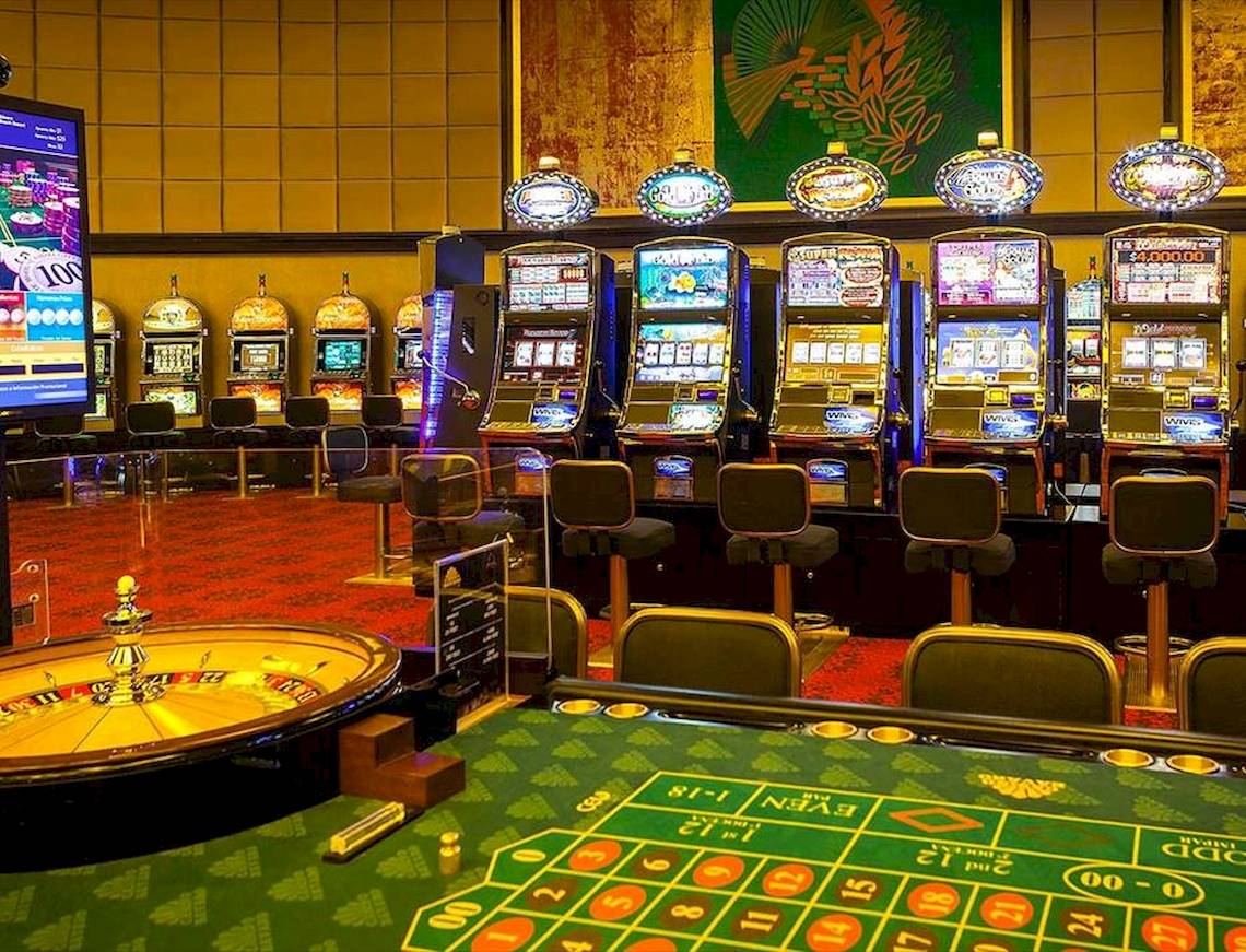 Innenbereich eines Casinos mit Spielautomaten, Roulettetisch und Stühlen.