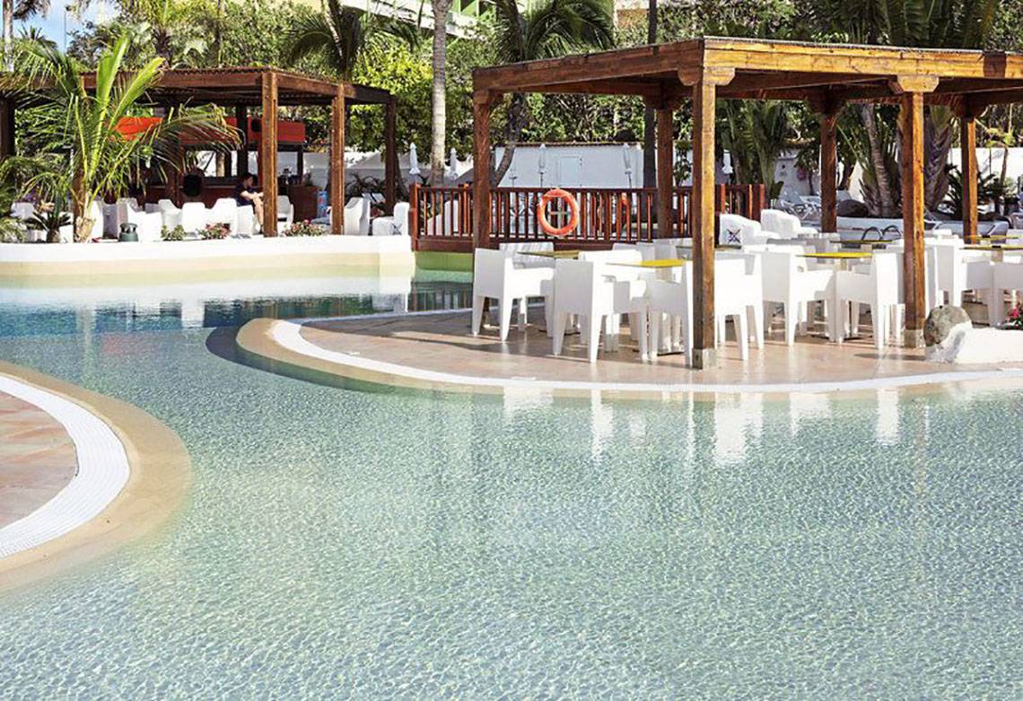 Poolbereich des Gran Canaria Princess Hotels mit weißen Stühlen und Tischen unter einem Holzpavillon.