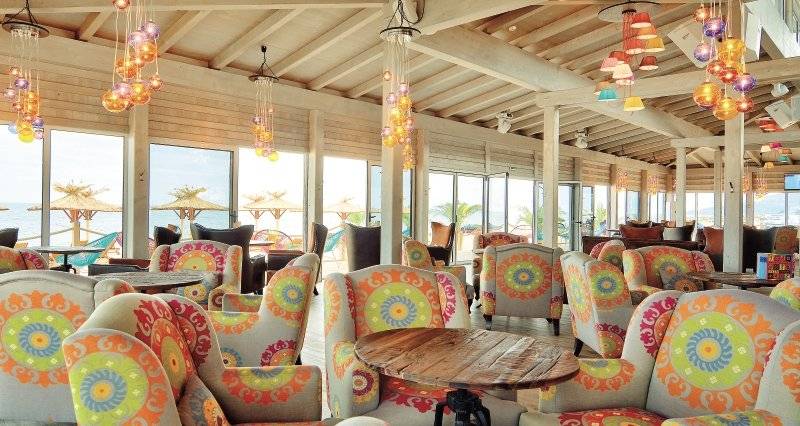 Innenansicht der Lounge im Kaliopa Hotel mit bunten Stühlen und Tischen am Meer