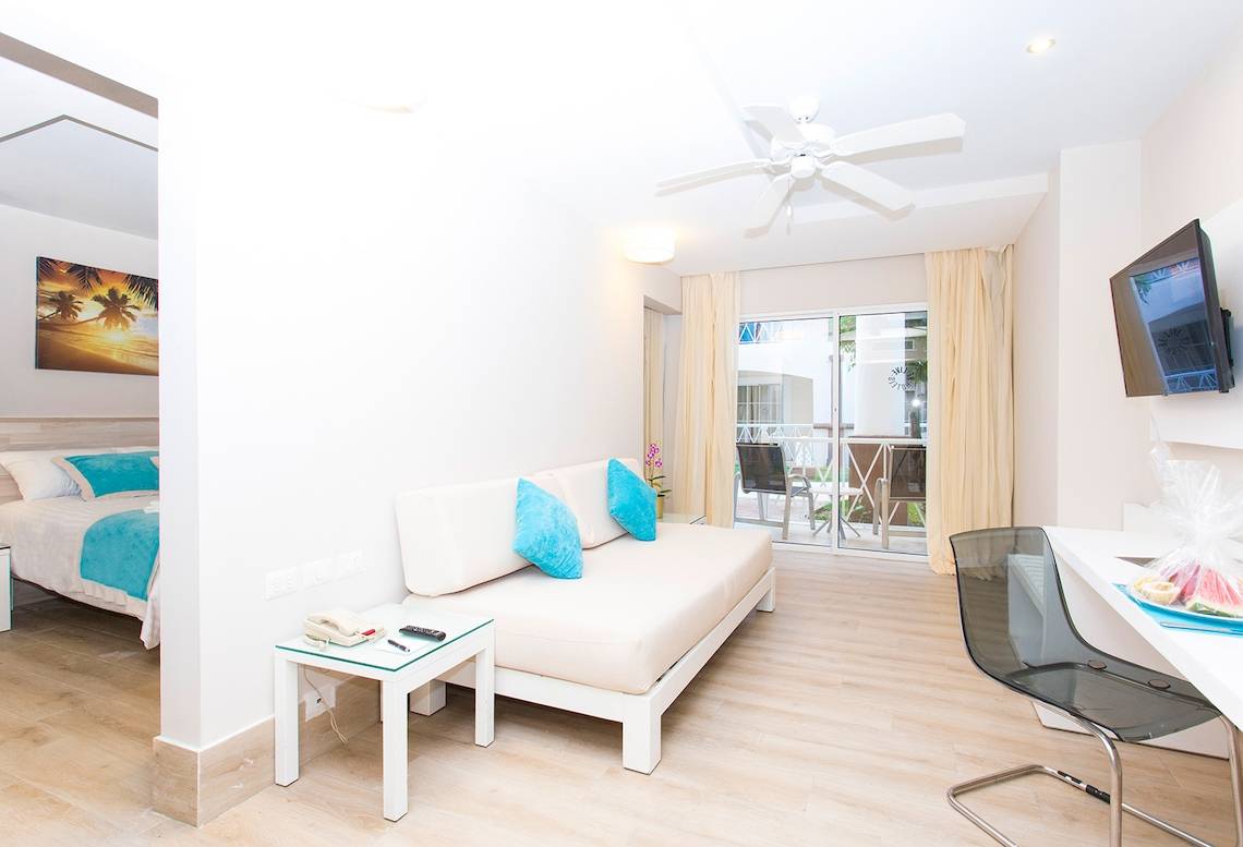 Innenansicht eines Zimmers im Sunscape Coco Punta Cana mit Bett, Sofa und Schreibtisch.