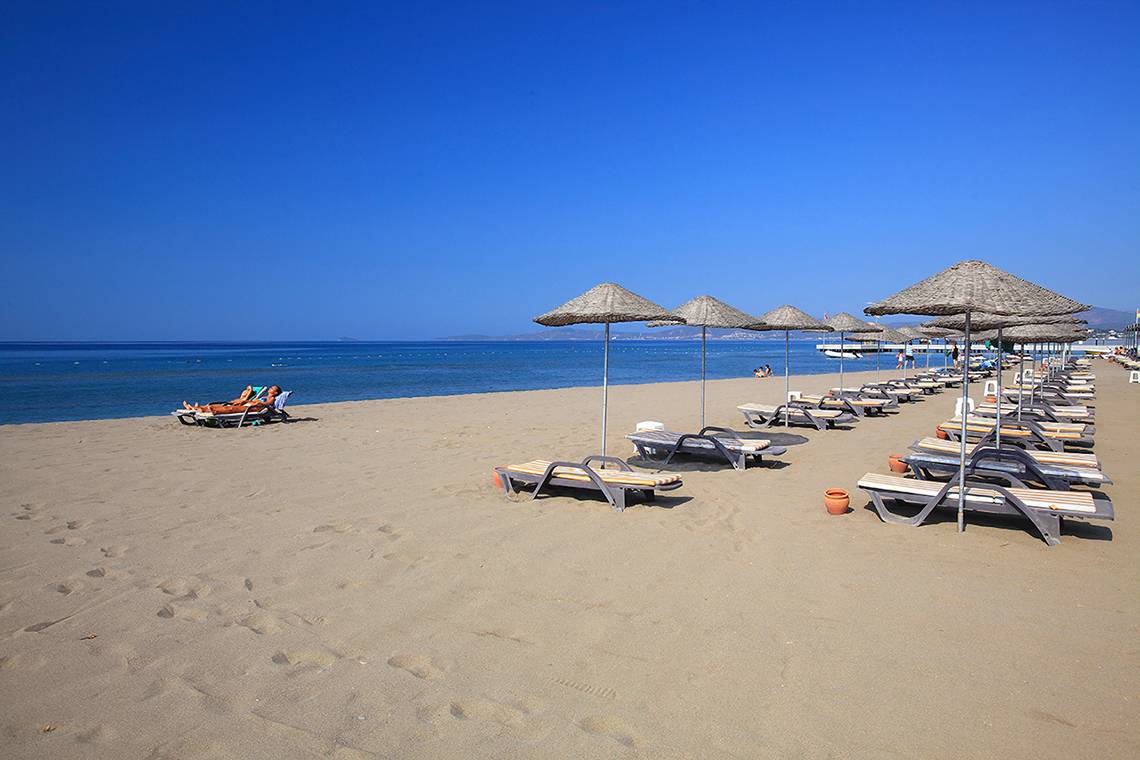 Strand des Club Yali Hotels & Resort mit vielen Sonnenliegen und Sonnenschirmen