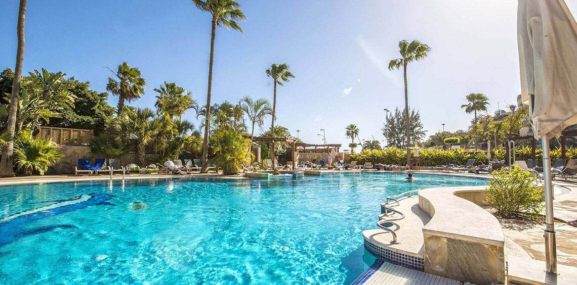 Außenpool des Corallium Dunamar Garden by Lopesan Hotels mit Palmen und Sonnenliegen.