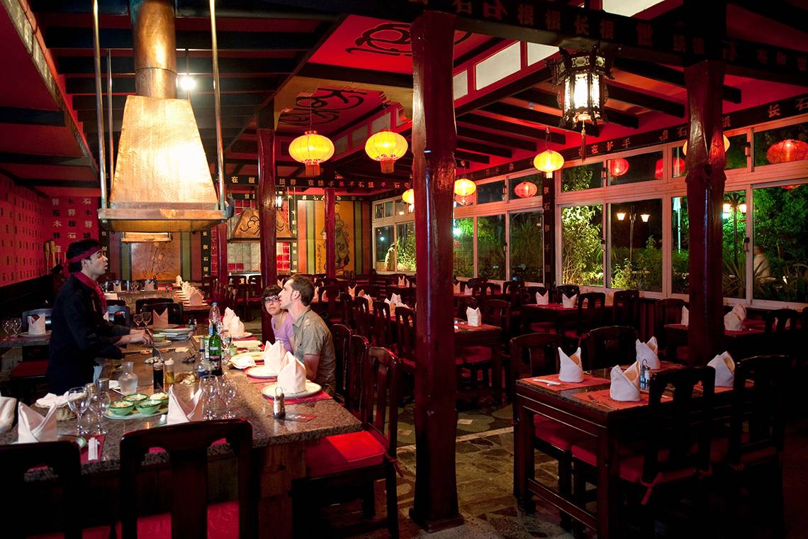 Innenbereich des Ghazala Beach Hotel Restaurants mit roten Stühlen und Tischen, hängenden Laternen und einem Kellner.