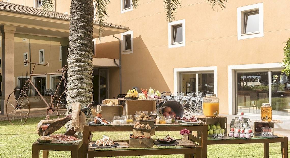 Frühstücksbuffet im Freien vor dem Occidental Playa de Palma Hotel mit Obst, Brot und Getränken.