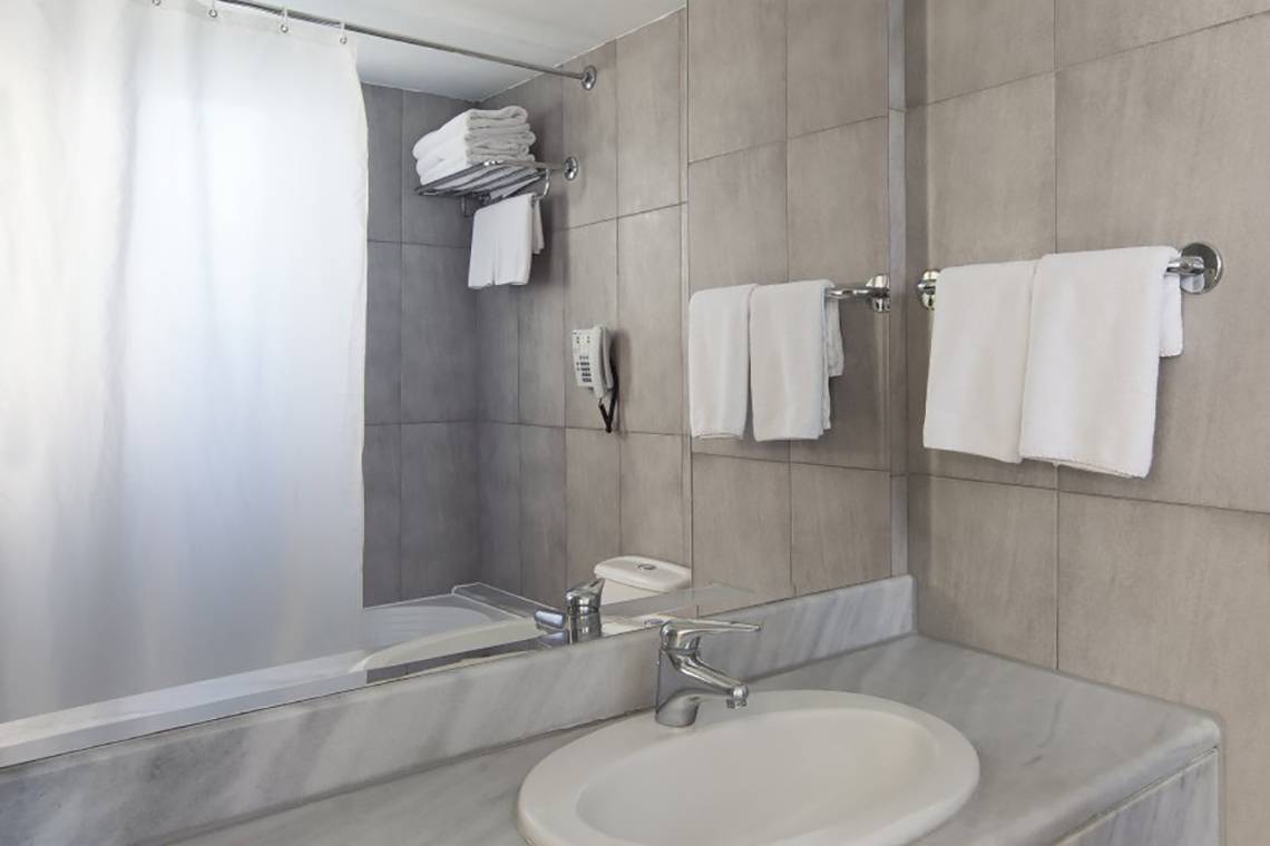 Badezimmer im Hotel Atlantica Mikri Poli auf Rhodos mit Spiegel, Waschbecken und Handtüchern.