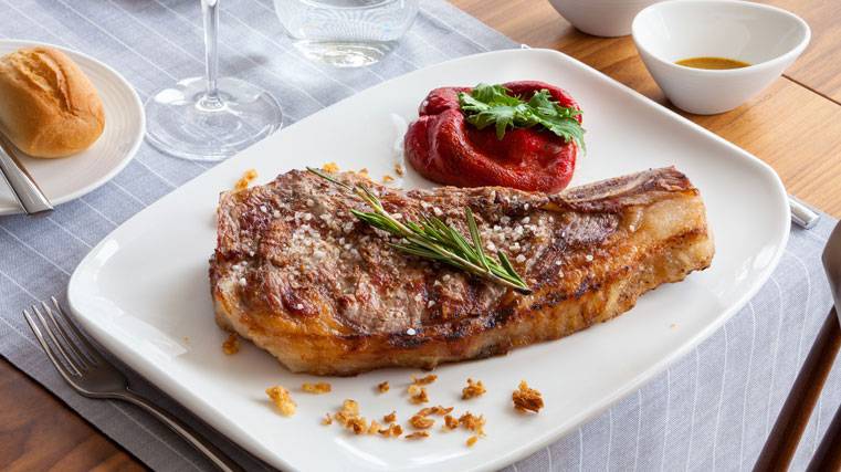 Gegrilltes Steak mit Rosmarin und roter Paprika auf weißem Teller.