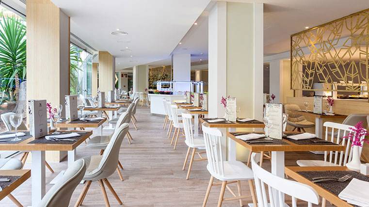 Innenansicht eines Restaurants im Hotel Tigotan Lovers & Friends mit Holztischen und weißen Stühlen.