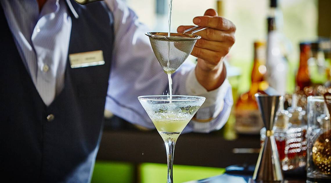 Ein Barkeeper bereitet einen Cocktail in einem Glas zu, indem er eine Flüssigkeit durch ein Sieb gießt.