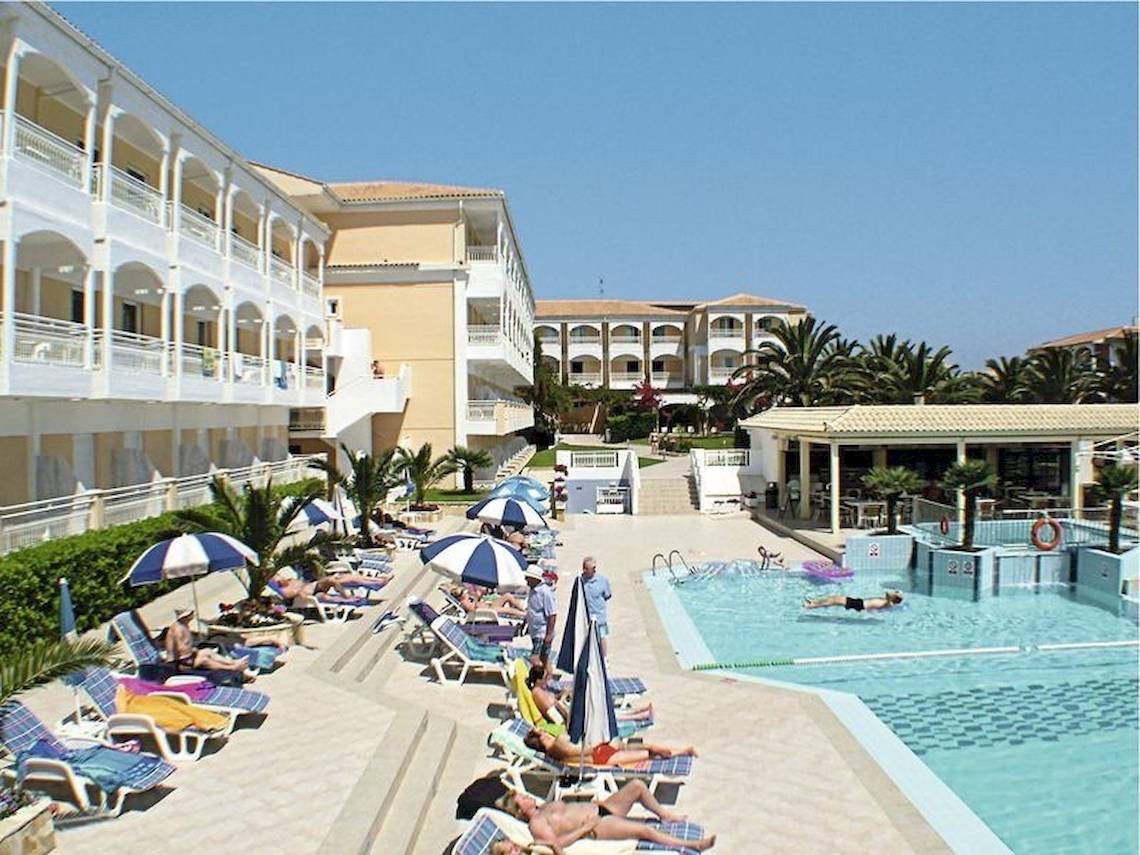 Außenbereich des Poseidon Beach Hotels mit Swimmingpool, Sonnenliegen und Sonnenschirmen.