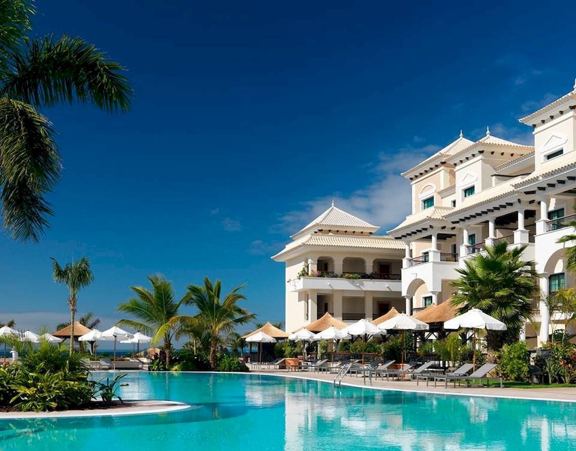 Außenpool des Gran Melia Palacio de Isora Hotels mit weißen Liegestühlen und Sonnenschirmen.